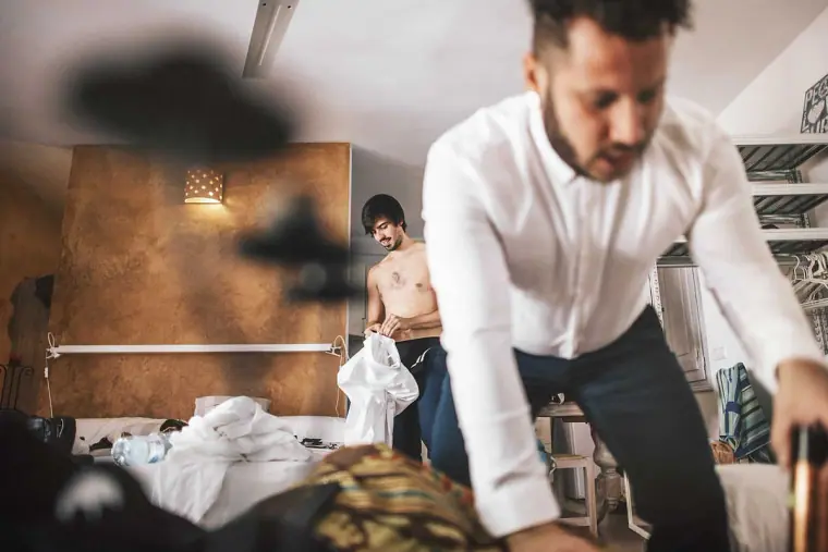 Groom in a white shirt getting dressed as a friend changes behind him