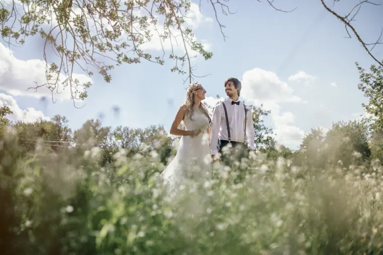 Bride and groom standing among tall wild grasses under trees