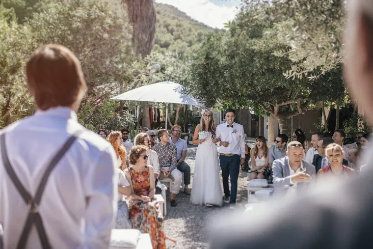 Groom in braces watching the bride walk down the garden aisle