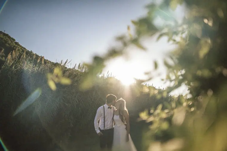 Couple standing in tall grass with the sun flaring through the leaves