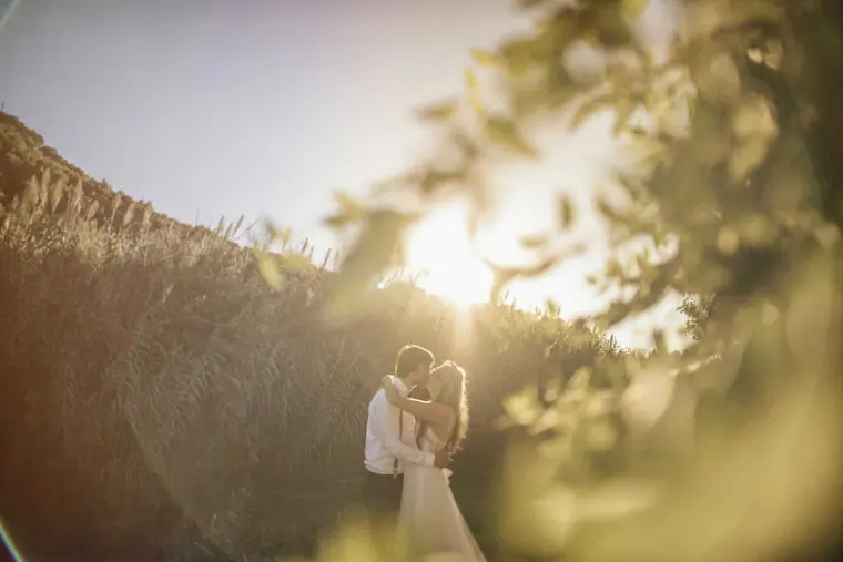 Couple kissing in tall grass with sunlight glowing behind them