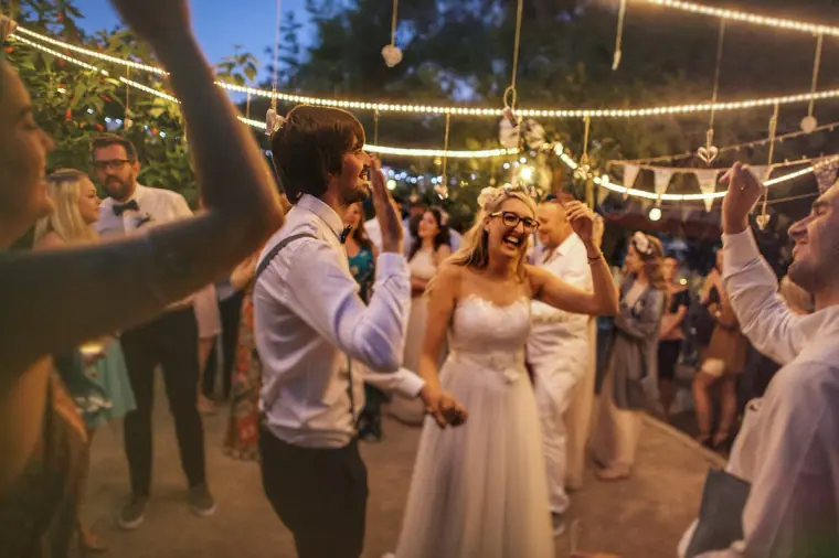 Bride and groom dancing among guests under strings of lights