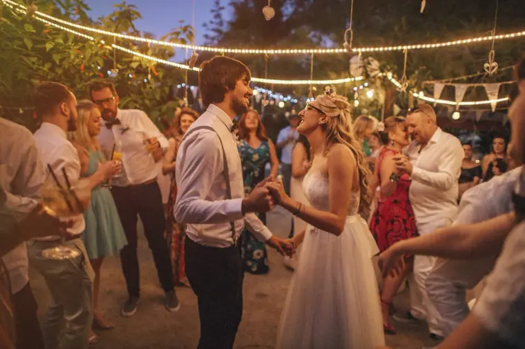 Guests dancing around the couple beneath string lights at dusk