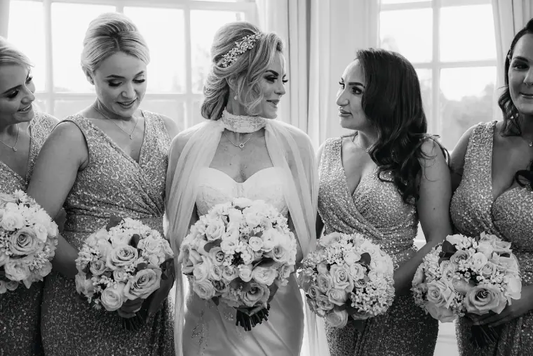 Black-and-white photo of Jade laughing with bridesmaids holding white rose bouquets