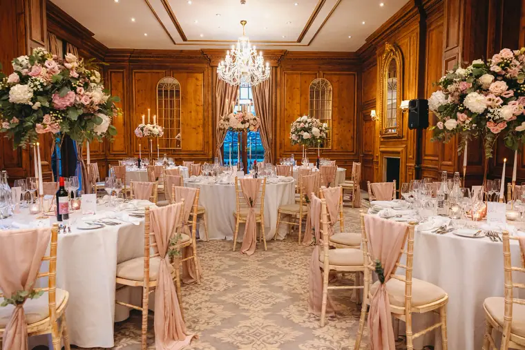 Wood-panelled dining room set with round tables, chandeliers and tall floral centrepieces