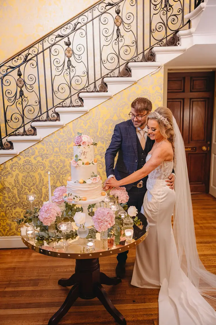Ian and Jade cutting their floral-decorated cake by the curving staircase