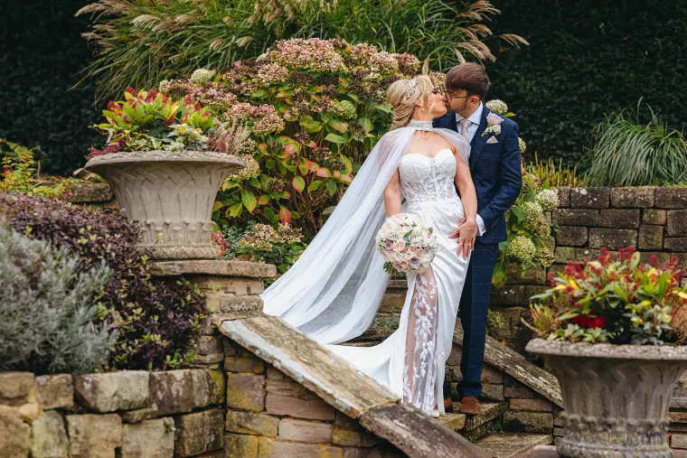 Ian and Jade kissing by stone urns on the garden steps
