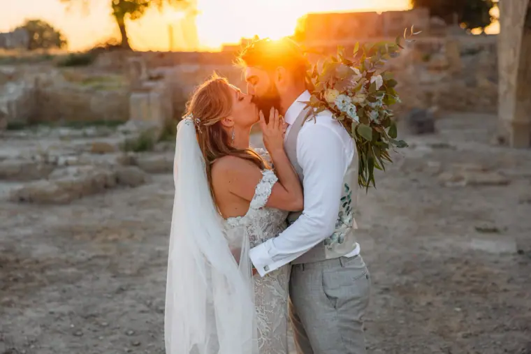 Bride and groom kissing among ancient stone ruins at sunset, Liopetro, Kouklia
