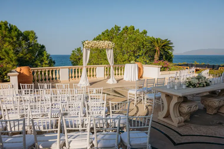 Ceremony terrace with white chairs and a floral arch overlooking the sea at Anassa Hotel
