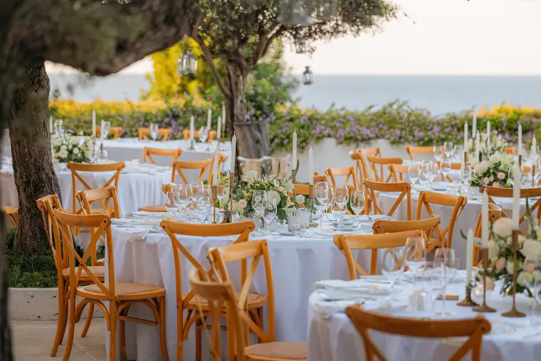 Garden reception laid out under olive trees with the sea beyond