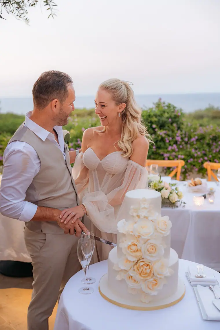 Jade and Peter laughing as they cut their sugar-rose wedding cake