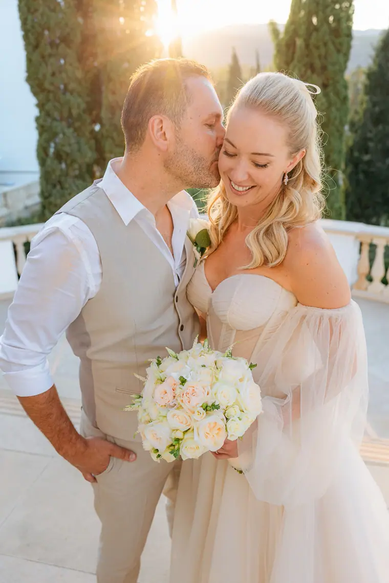 Jade smiling with her rose bouquet as Peter kisses her cheek