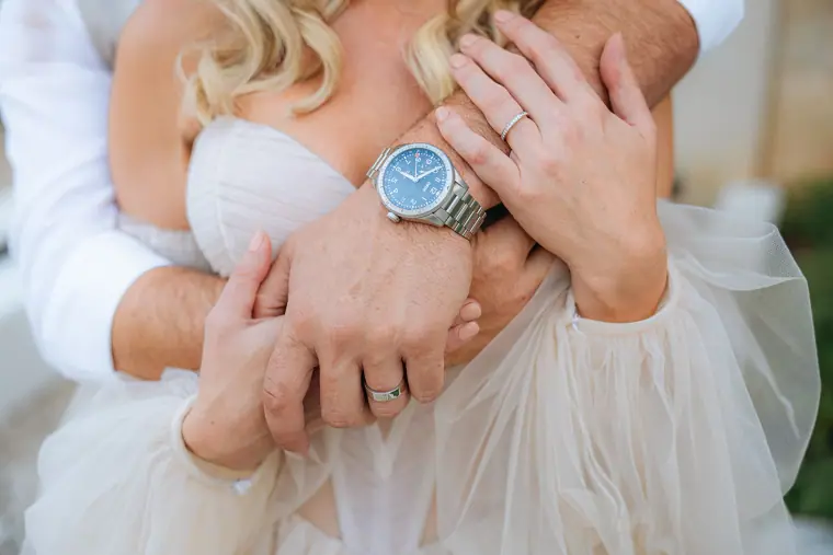 Close-up of the couple's hands, wedding rings and watch on her tulle sleeve