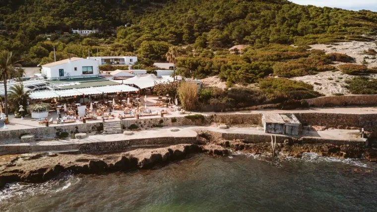 Beachfront restaurant La Escollera on a rocky cove with turquoise water and pine-covered hills, Ibiza