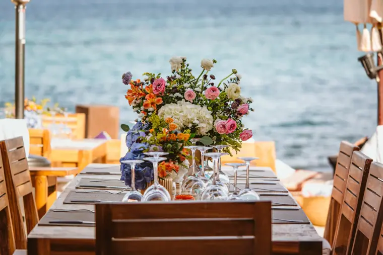 Colourful bouquet and glassware on a long wooden table facing the sea at La Escollera, Ibiza