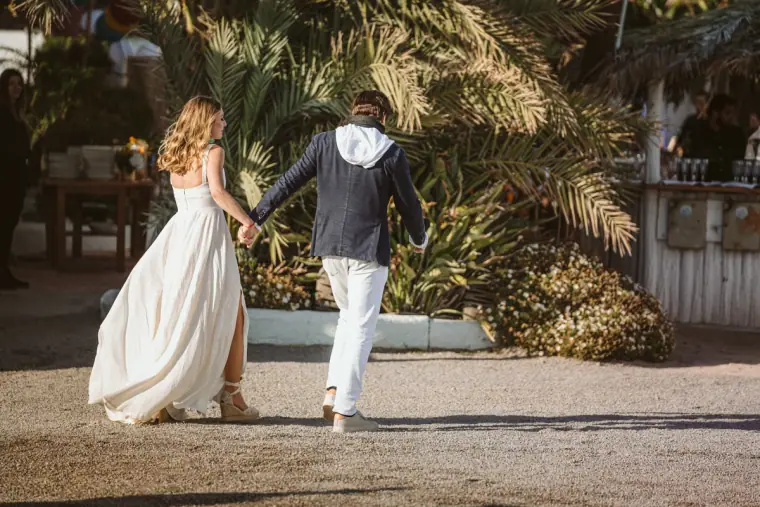 Bride and groom walking hand in hand past palm trees at La Escollera, Ibiza