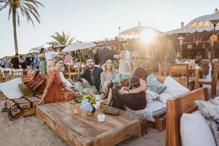 Guests relaxing on cushioned lounge seating on the sand in the late afternoon sun