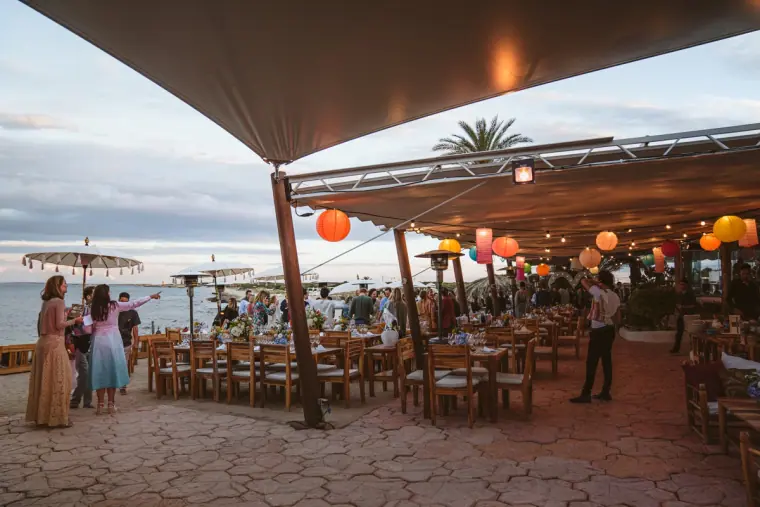 Guests mingling beneath a large canopy hung with colourful lanterns on the seafront terrace