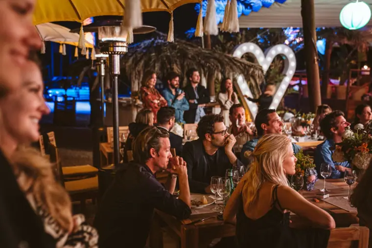 Guests seated at candlelit tables under a glowing heart sign at the evening party, La Escollera, Ibiza