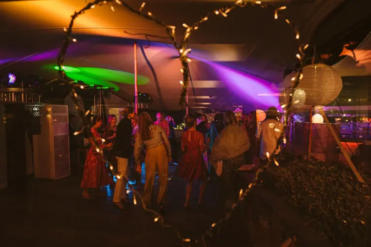 Dance floor under a tent strung with fairy lights and purple uplighting at night