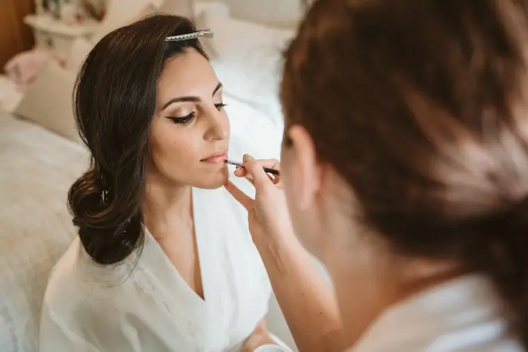 Makeup artist applying lipstick to the bride during getting ready