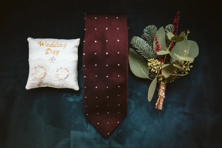 Wedding Day ring cushion, burgundy tie and pine buttonhole laid on blue velvet