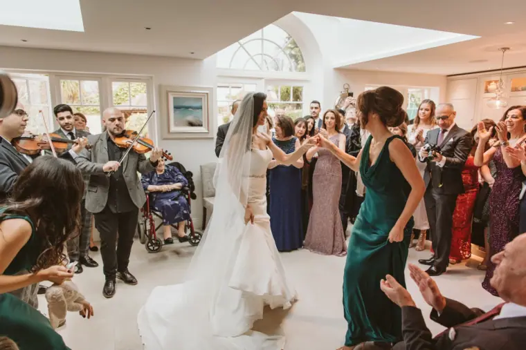 Bridesmaid dancing with the bride to live violin music in a crowded room