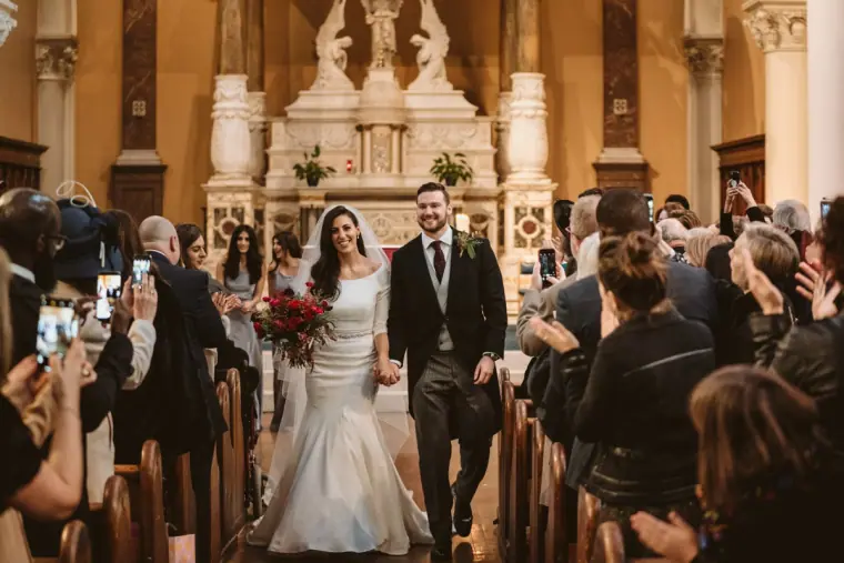 Stephanie and Jamie walking back down the aisle as newlyweds past cheering guests