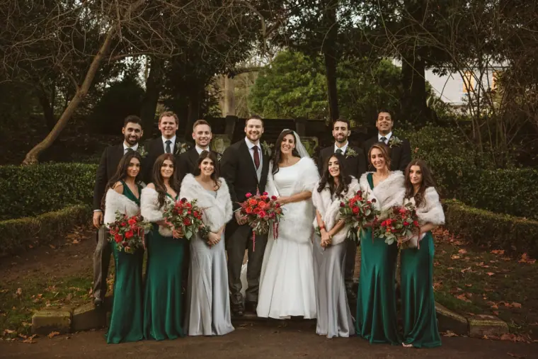 Bride and groom with bridesmaids in emerald and silver and groomsmen in a London garden