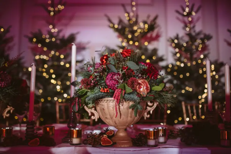 Urn of red roses and protea between candles and fairy-lit Christmas trees on the reception table