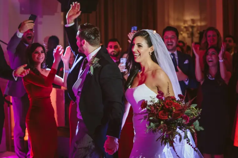 Bride with red bouquet dancing among cheering guests at the reception