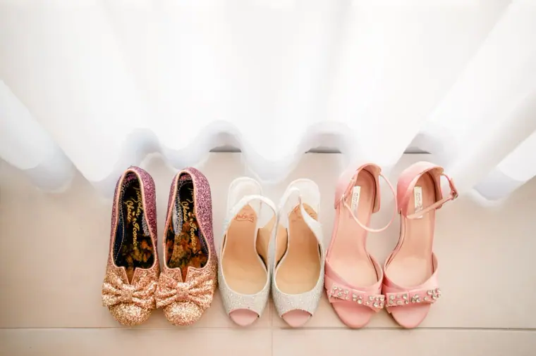 Row of bridal shoes in glitter, ivory and blush pink lined up beneath a window