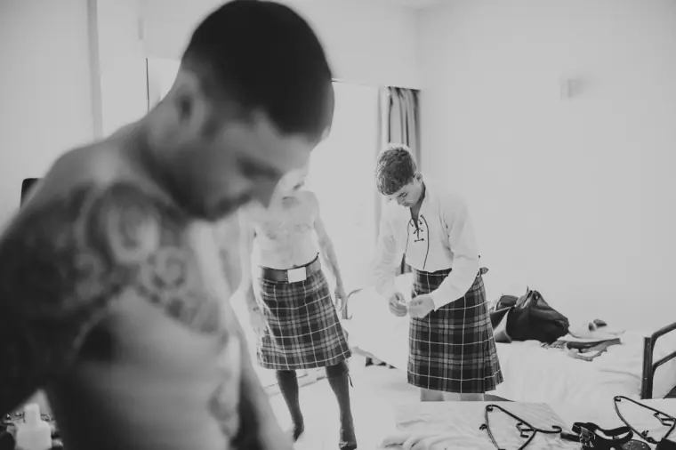 Black-and-white photo of the men getting ready in kilts in a hotel room