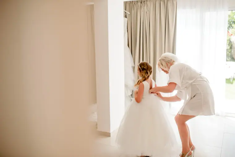 Mother helping the flower girl into her full white tulle dress