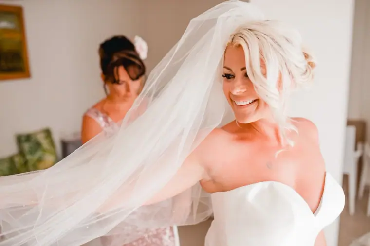Smiling bride adjusting her long veil with a bridesmaid behind her