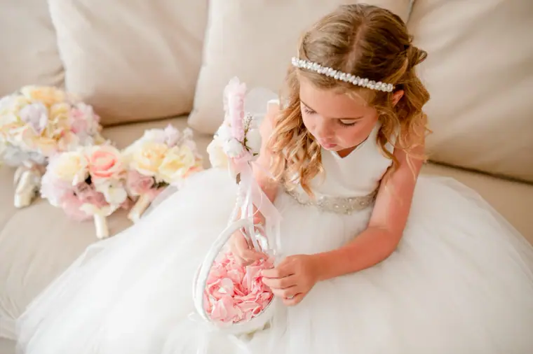Flower girl with a pearl headband holding a basket of pink petals beside pastel bouquets