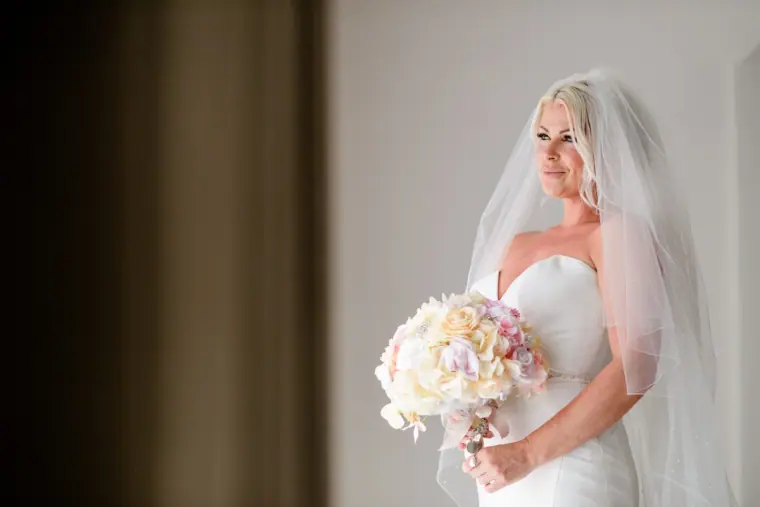 Bride in a strapless gown and veil smiling down at her bouquet