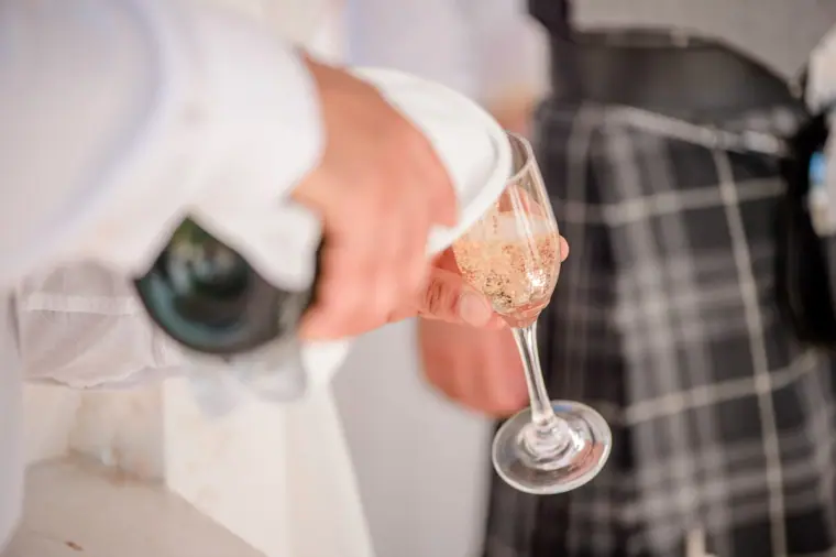 Close-up of a glass of fizz being poured beside a tartan kilt