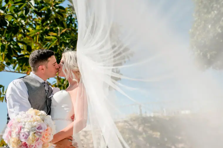 Couple kissing as her long veil floats across the frame in the sea breeze