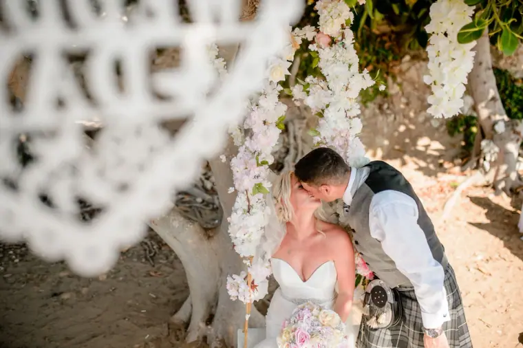 Couple kissing beneath a blossom arch, framed by a lace parasol