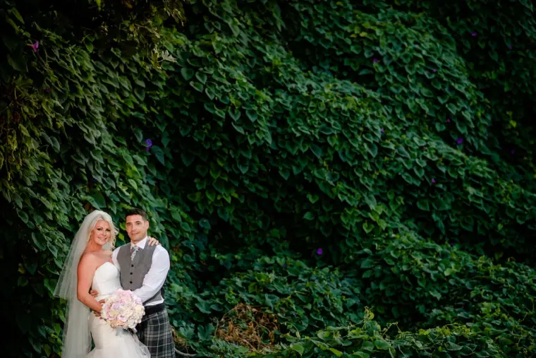 Bride and groom standing before a wall of dense green ivy