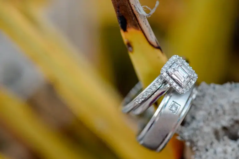 Diamond engagement ring and wedding bands balanced on a rock among leaves
