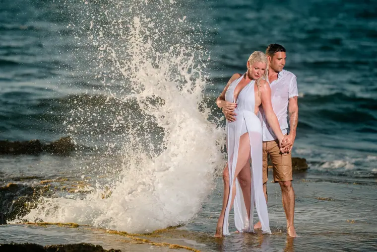 Wave crashing beside the couple as they pose on wet rocks at the shoreline