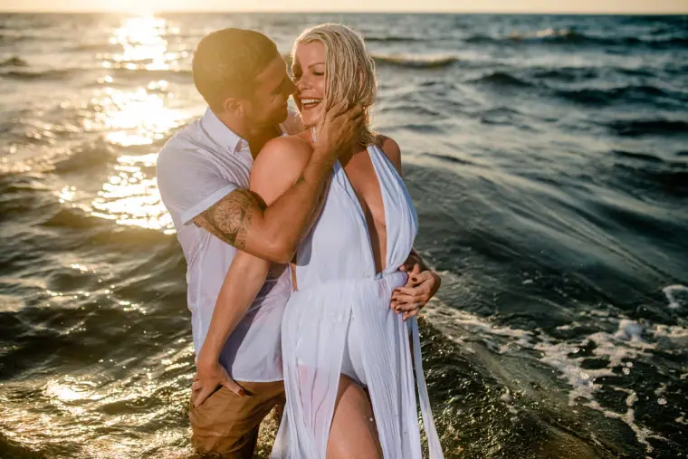 Ben and Maryellen embracing in the sea with sunlight glinting on the water