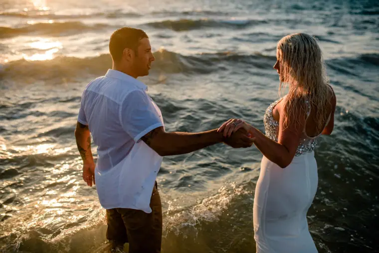 Couple holding hands as they wade into the sea at sunset