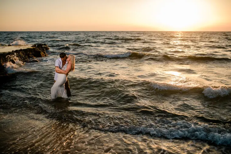 Couple embracing in the sea at sunset, the sun low over the water