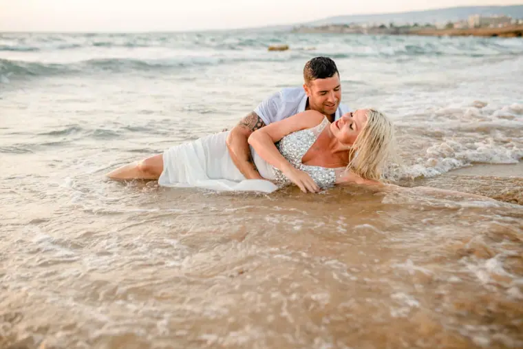 Couple lying together at the water's edge as waves wash over them