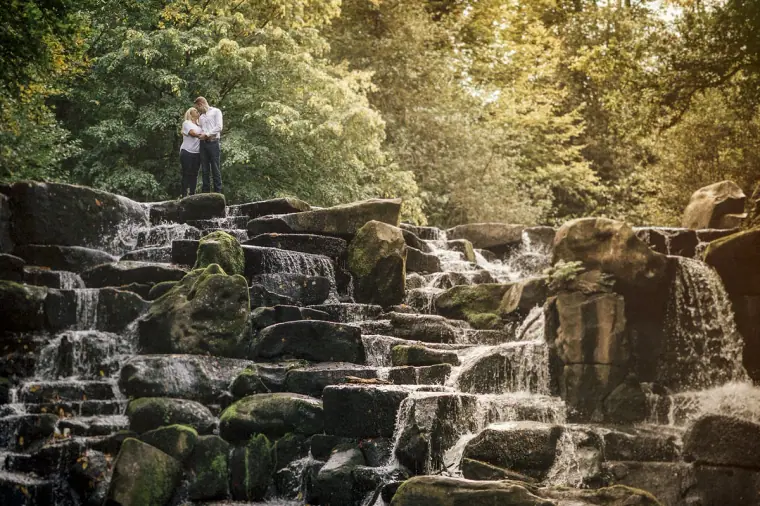 Couple embracing at the top of the stepped rocky waterfall surrounded by woodland