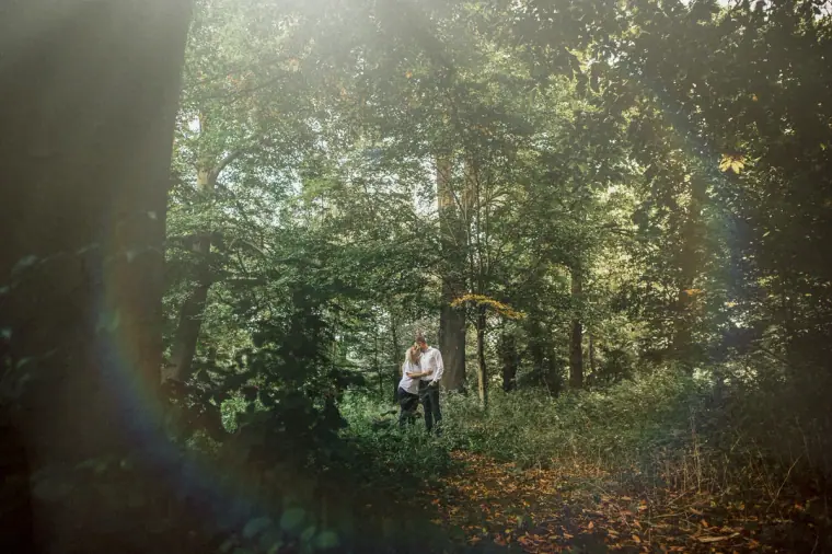 Couple standing small in a sunlit woodland clearing with a lens flare