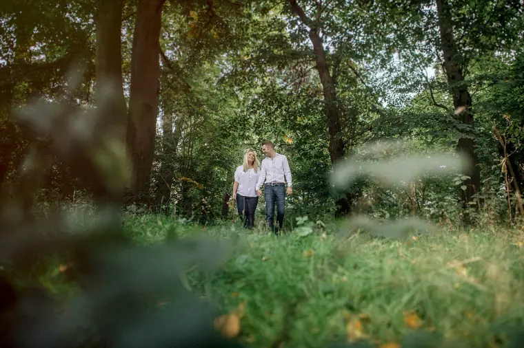 Lauren and Anthony walking hand in hand through long grass under tall trees